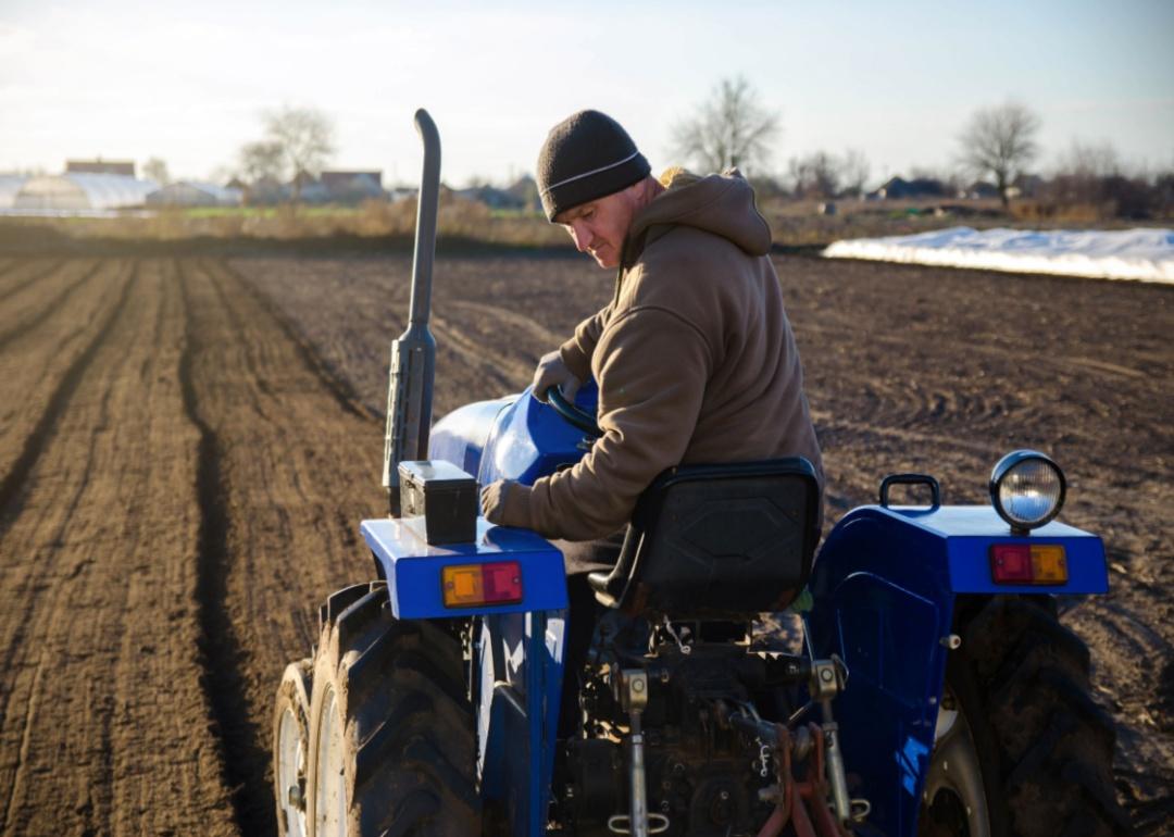 A man in a field on a small blue tractor.