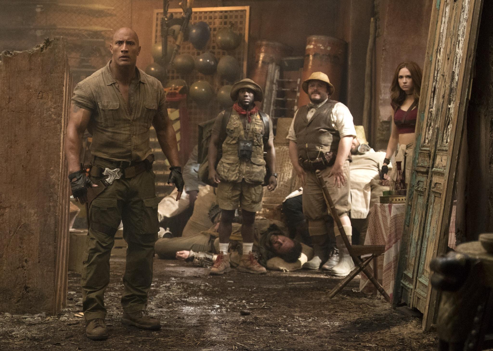 Jack Black, Kevin Hart, Dwayne Johnson, and Karen Gillan stand looking surprised in a destroyed room.