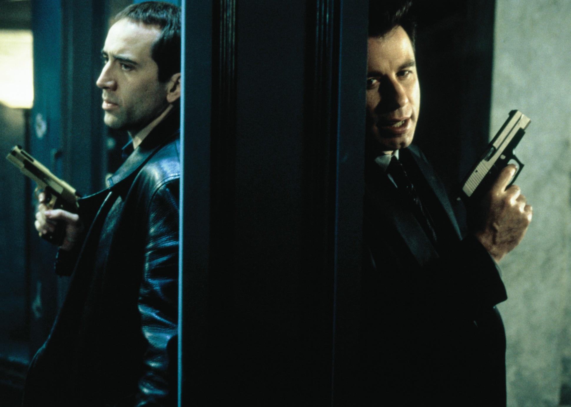 Nicolas Cage and John Travolta, both holding guns, stand back to back against walls.