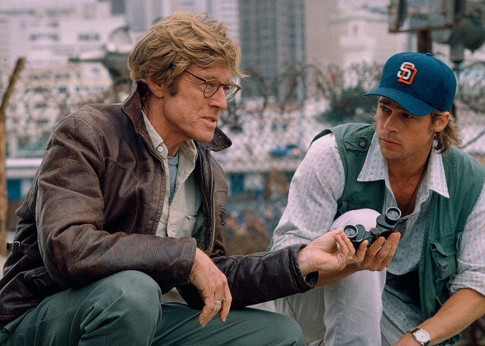 Brad Pitt and Robert Redford crouched down with a pair of binoculars.
