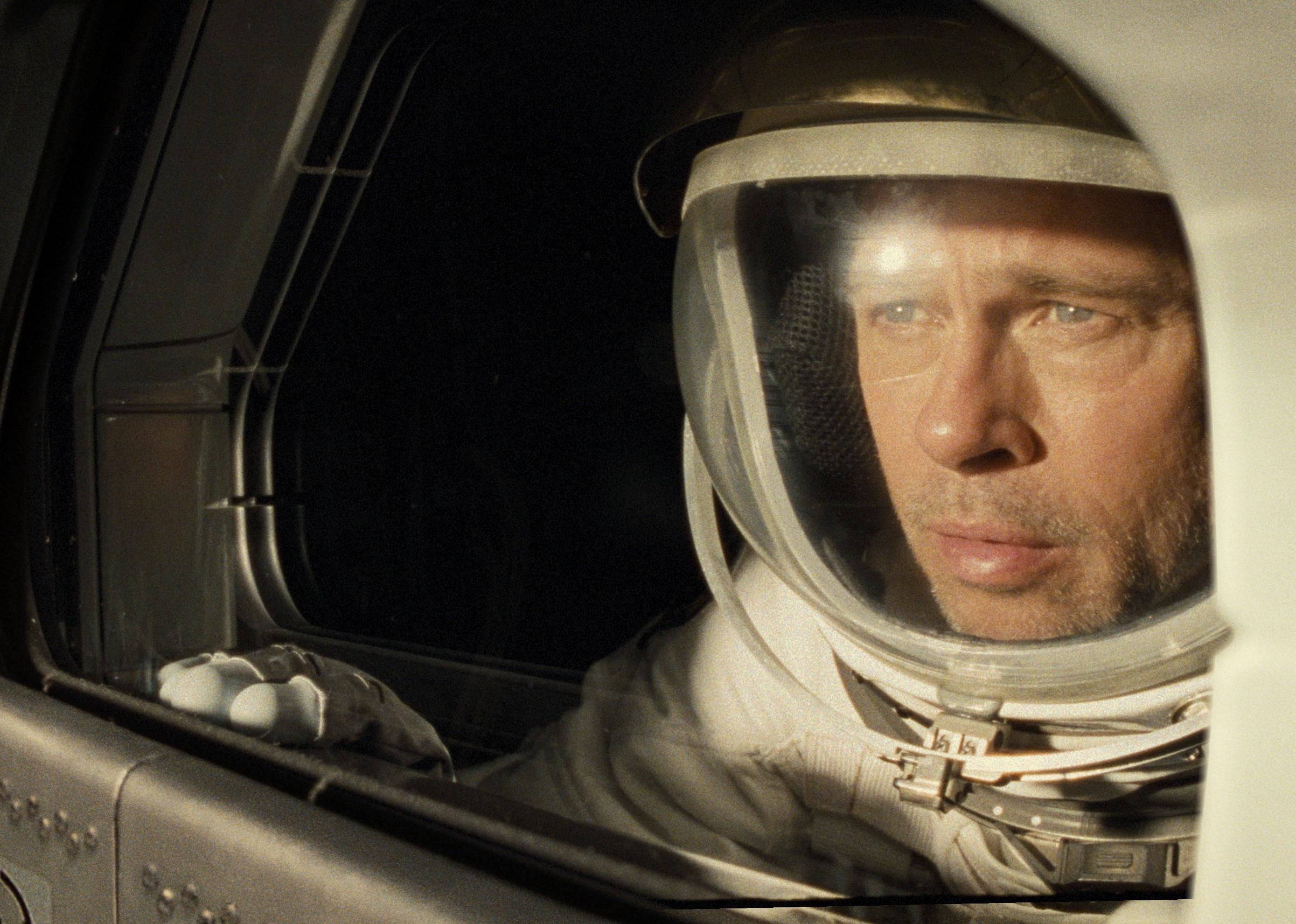 Brad Pitt in a spacesuit looking out the window of a spaceship.