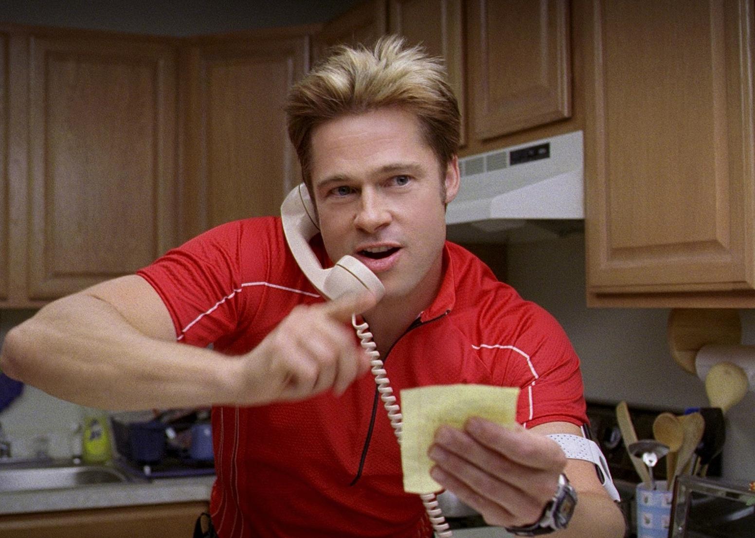 Brad Pitt in a red track suit talking energetically on the phone.