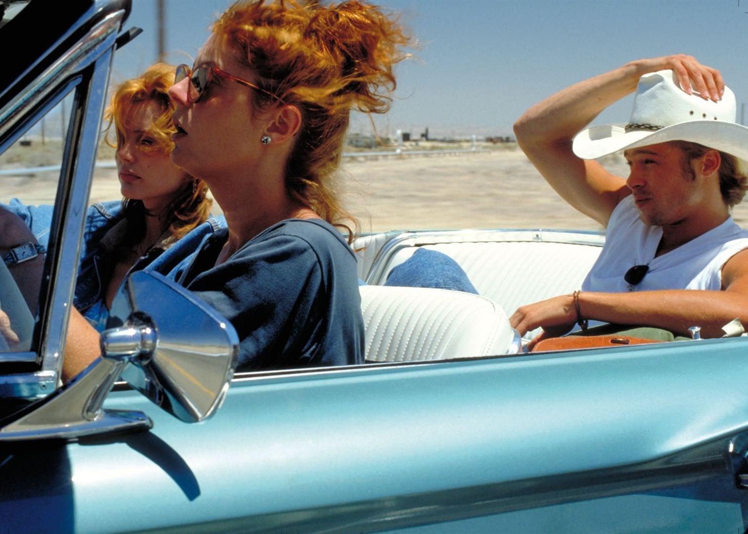 Brad Pitt in a cowboy hat riding in the back of a convertible with Geena Davis and Susan Sarandon in the front.
