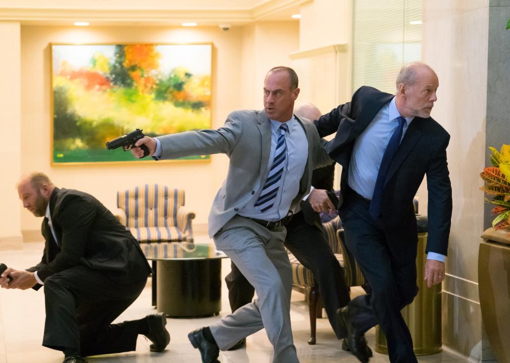 Men in suits and ties point guns while trying to escape a room.