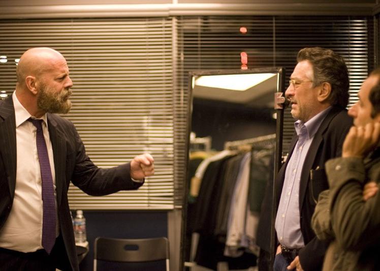 A bearded man in a suit argues with a man in glasses and a jacket.