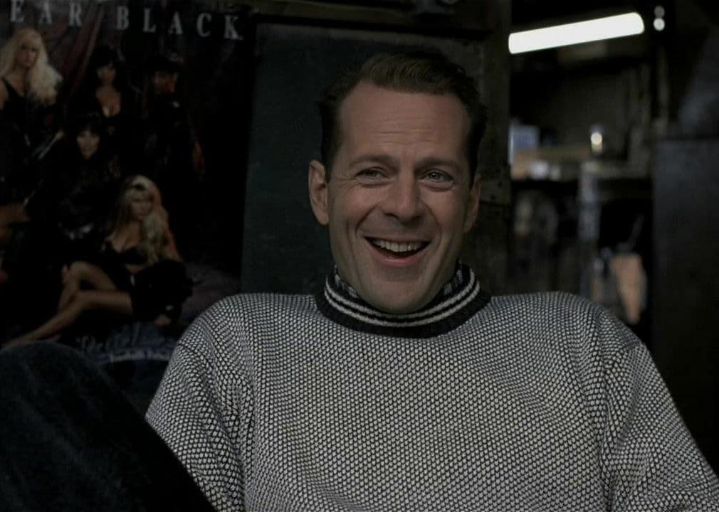 Bruce Willis sits in a chair laughing.