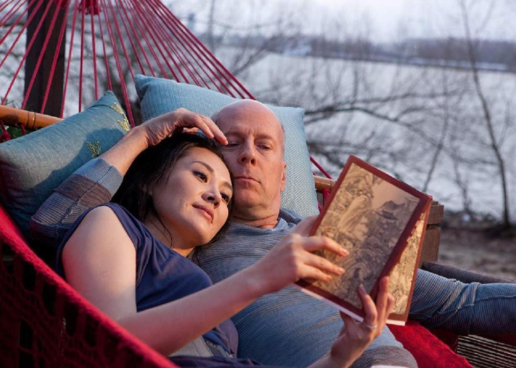 A man and woman lay in a hammock reading a book together.