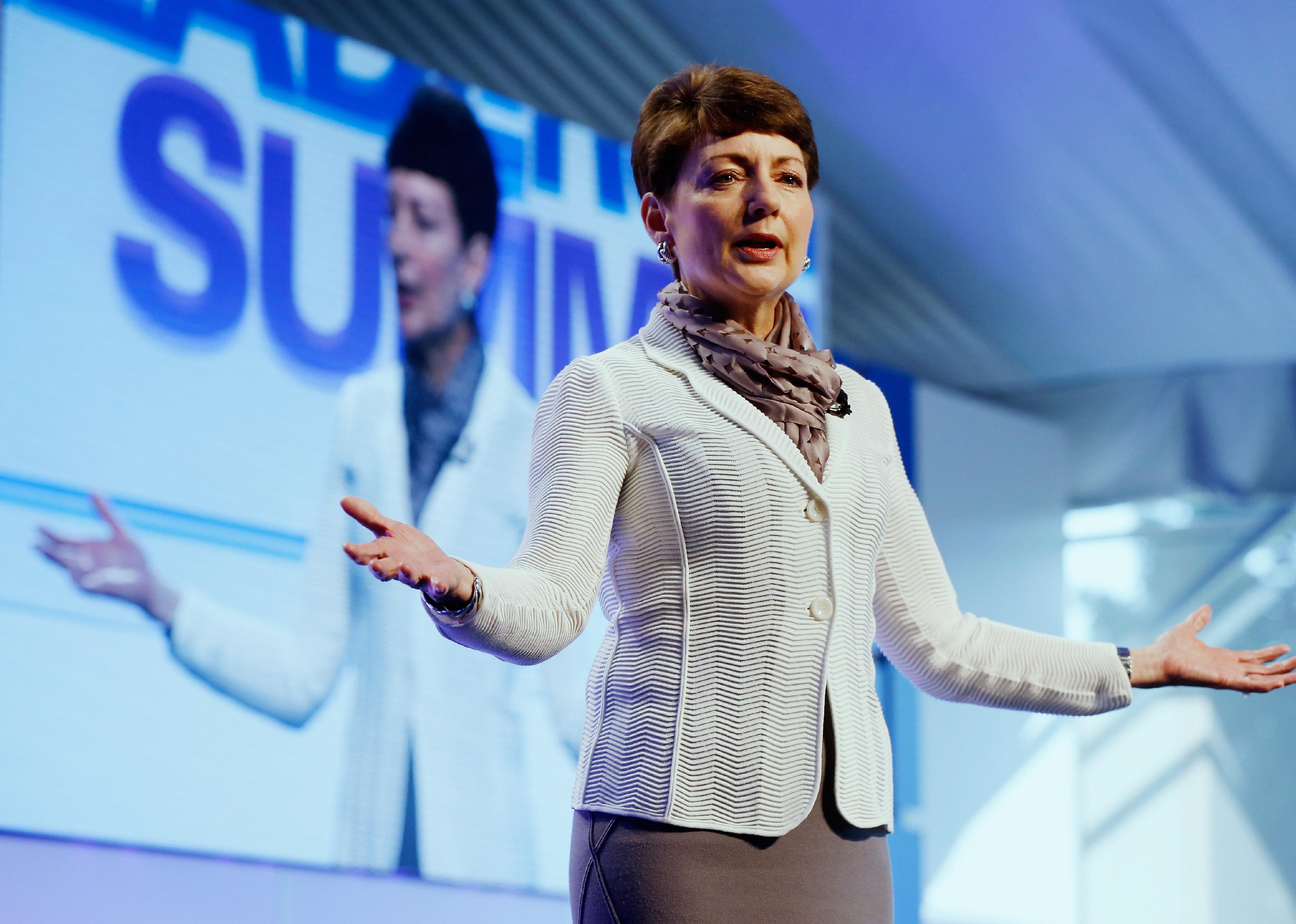 Lynn good speaking onstage with a blue screen behind her.