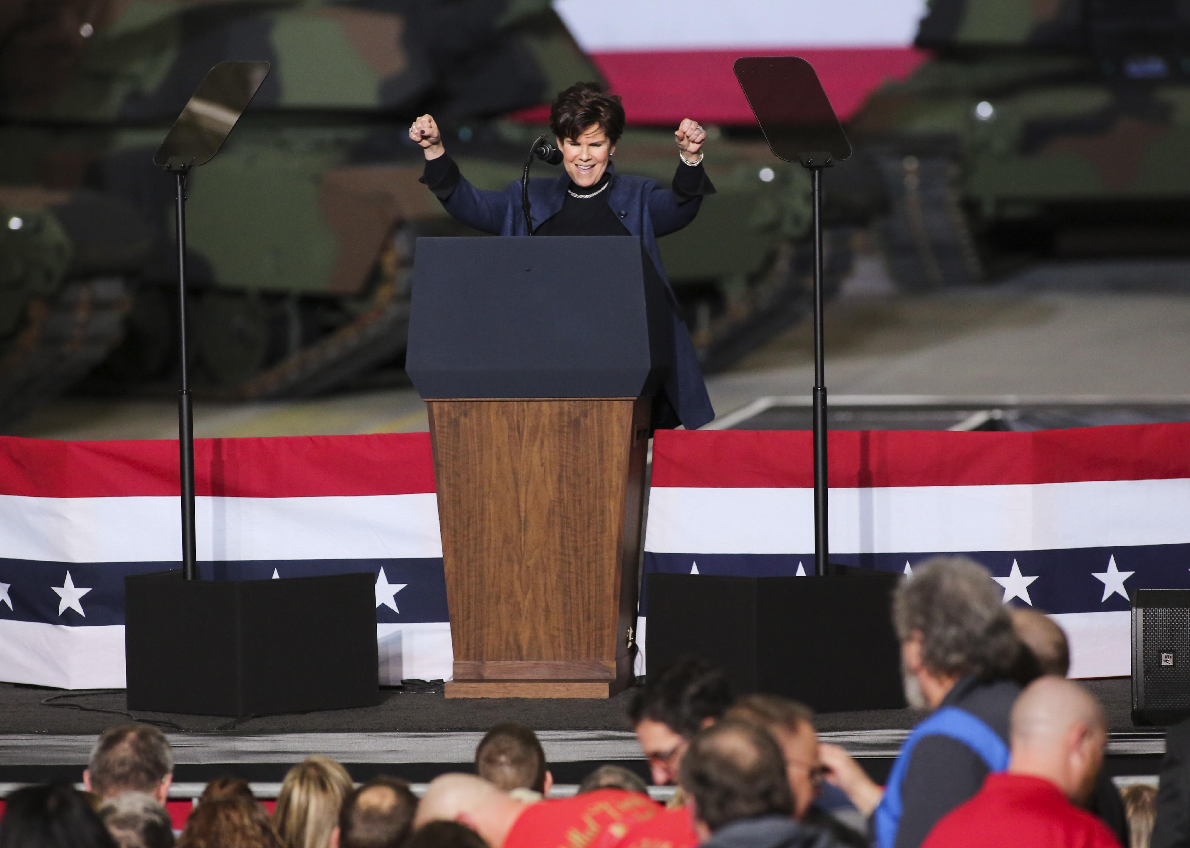 Phebe Novakovic speaks and cheers on a stage decorated with stars and stripes.