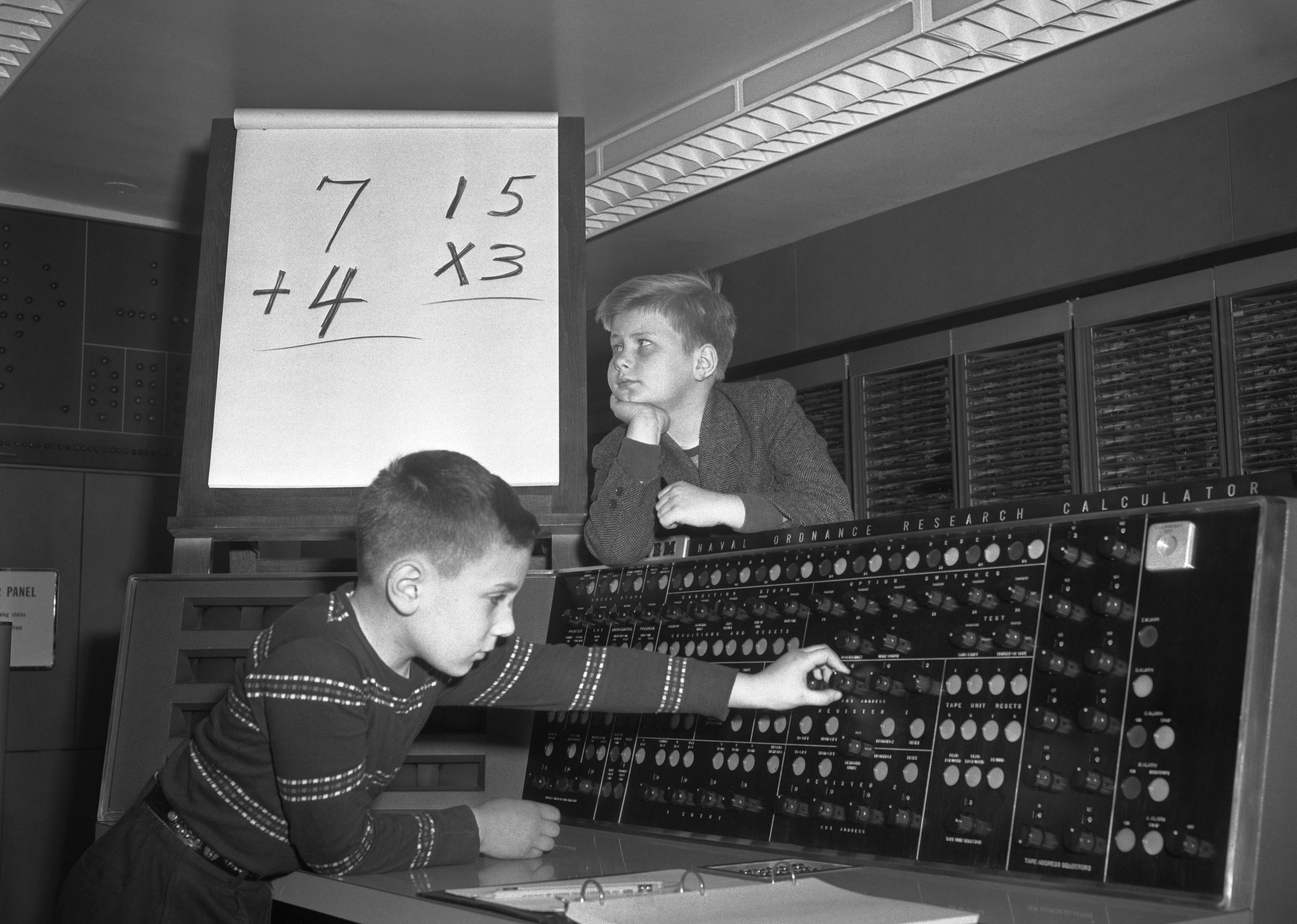 Two young boys brainstorm an equation while playing on a giant electronic calculator at IBM.