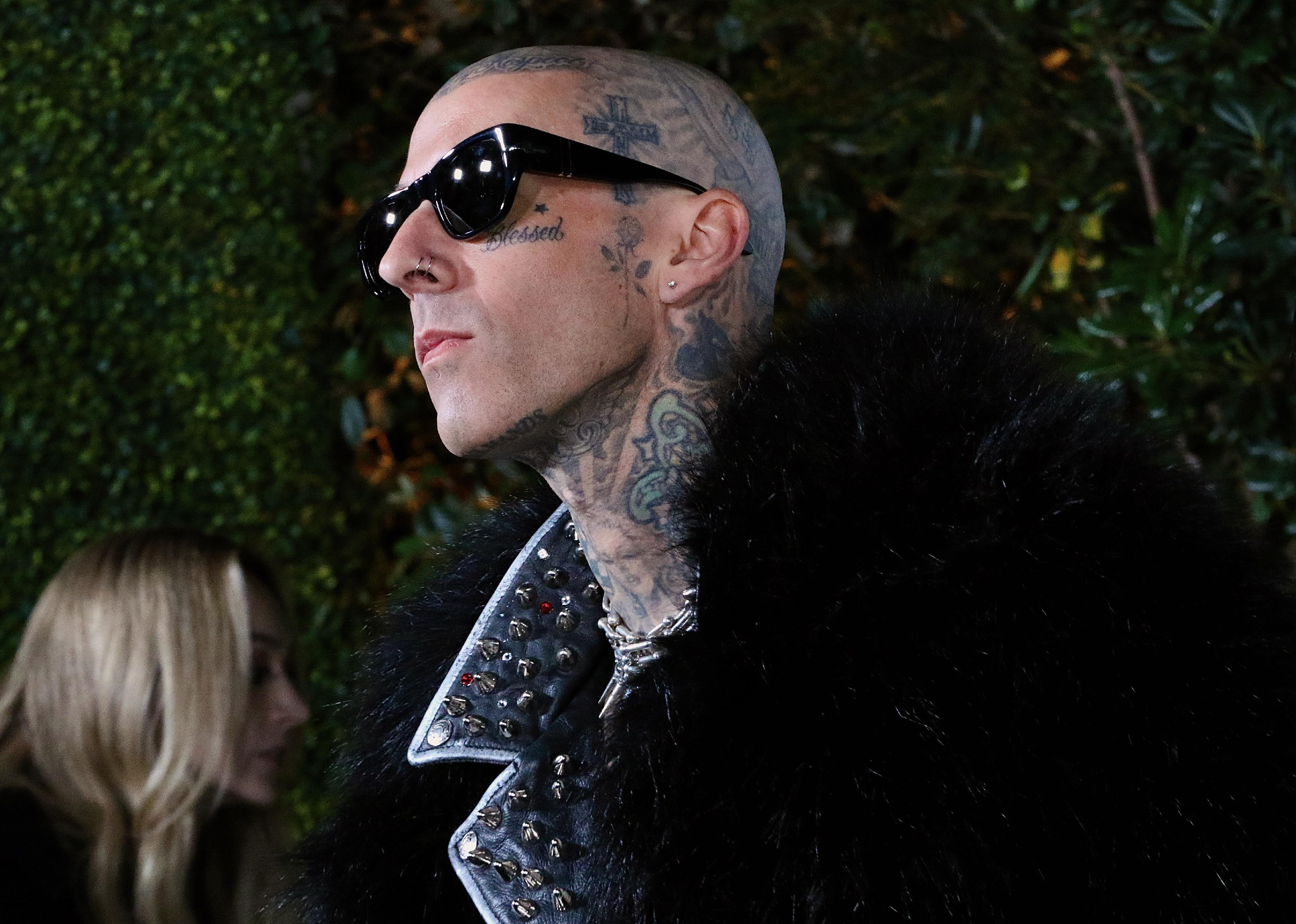 Travis Barker in dark sunglasses and a black fur coat.