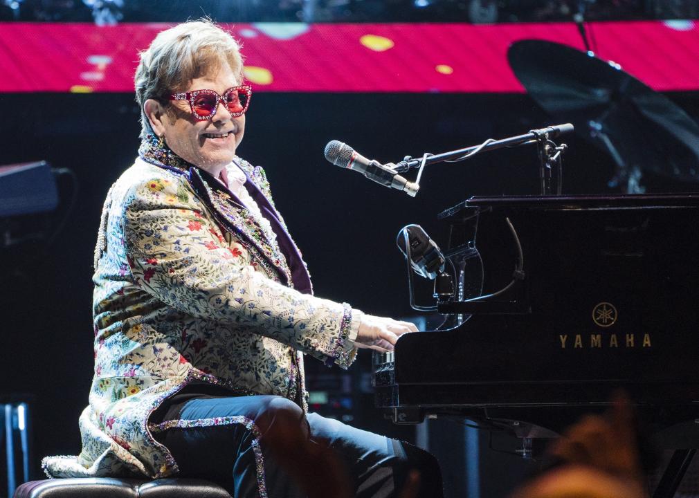 Elton John playing the piano in a floral jacket and sparkly sunglasses.
