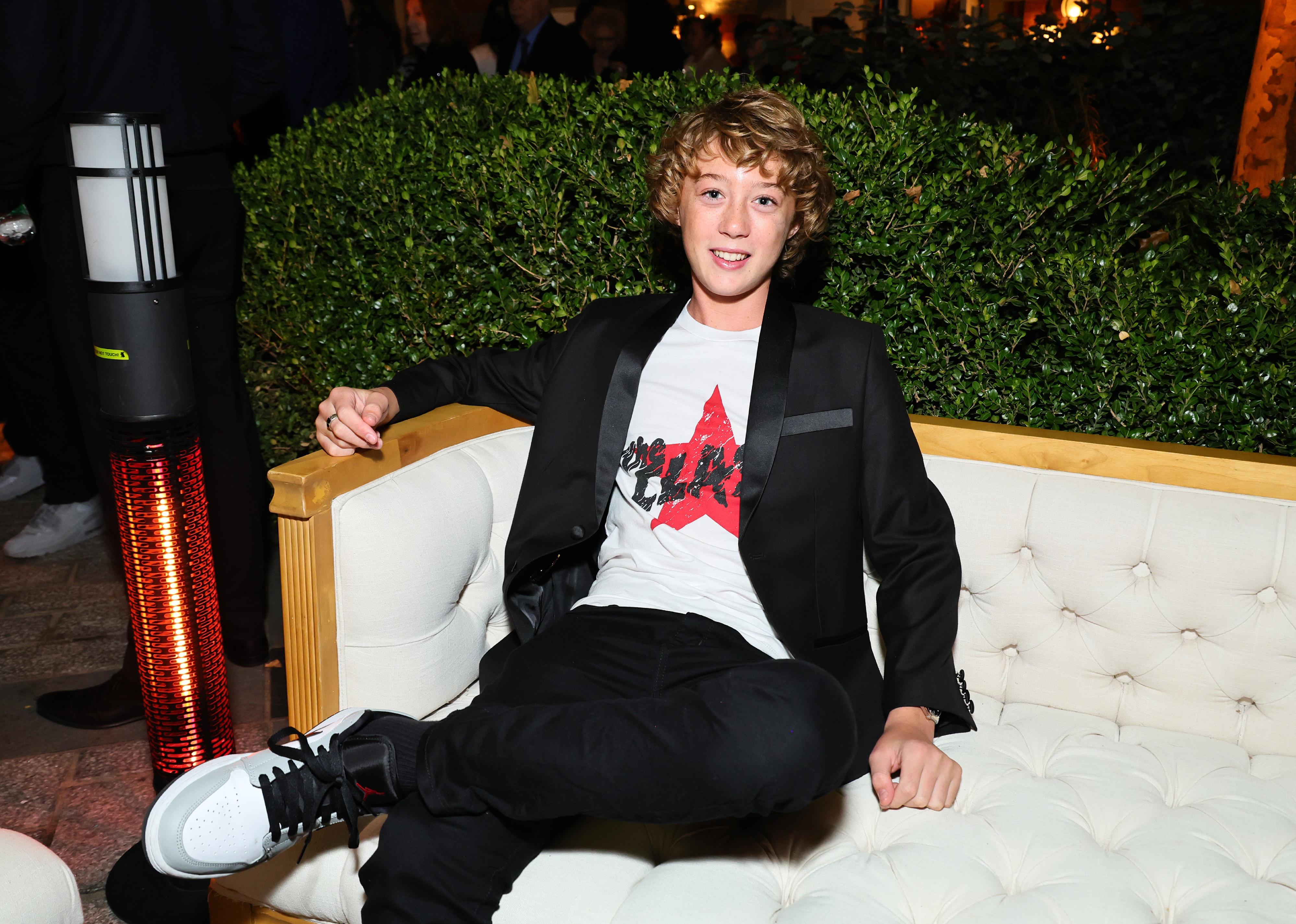 Banks Repeta in a black suit and t-shirt on a couch.