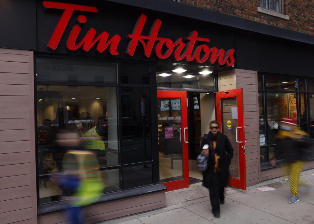 A slightly blurred woman walks out of a Tim Hortons carrying a to-go cup. 