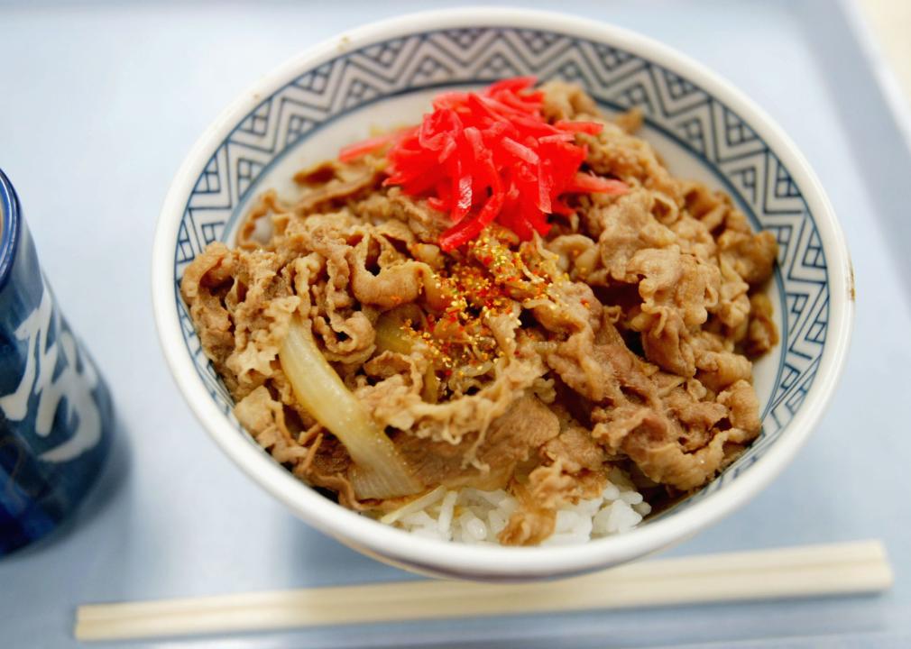 A beef and rice bowl with chopsticks next to it. 