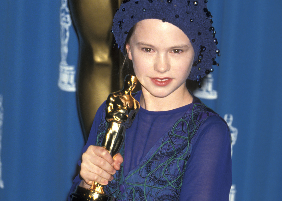 Anna Paquin in a purple dress and hat holding an Academy Award.