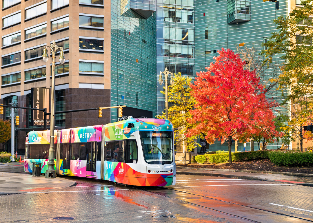 A colorful city tram in downtown with fall trees and buildings in the background.