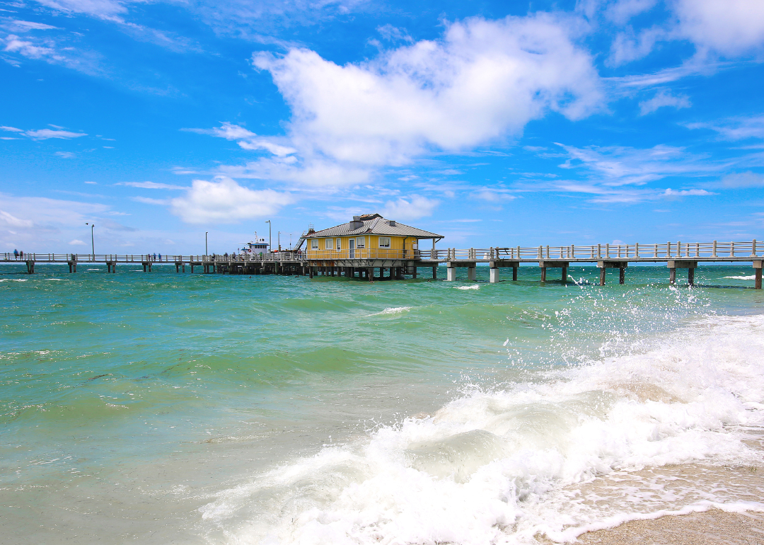 A long pier going out into turquoise water on the beach.