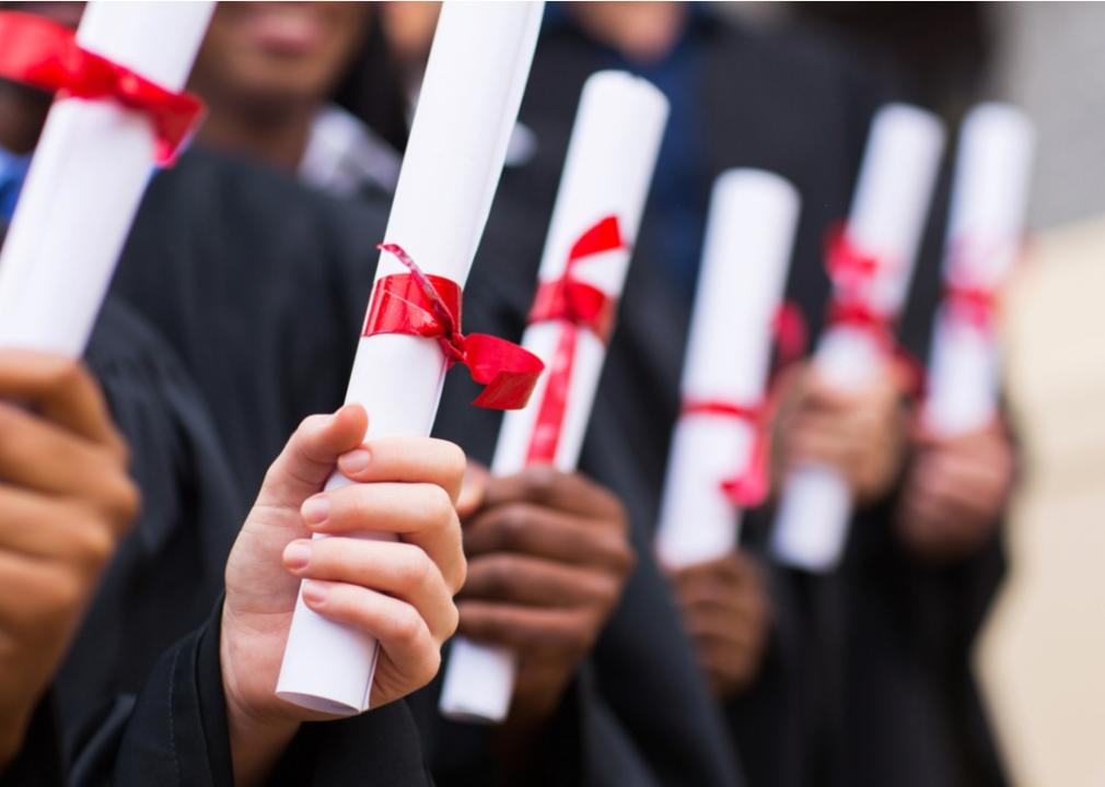 Students in caps and gowns hold their diplomas wrapped in red ribbons.