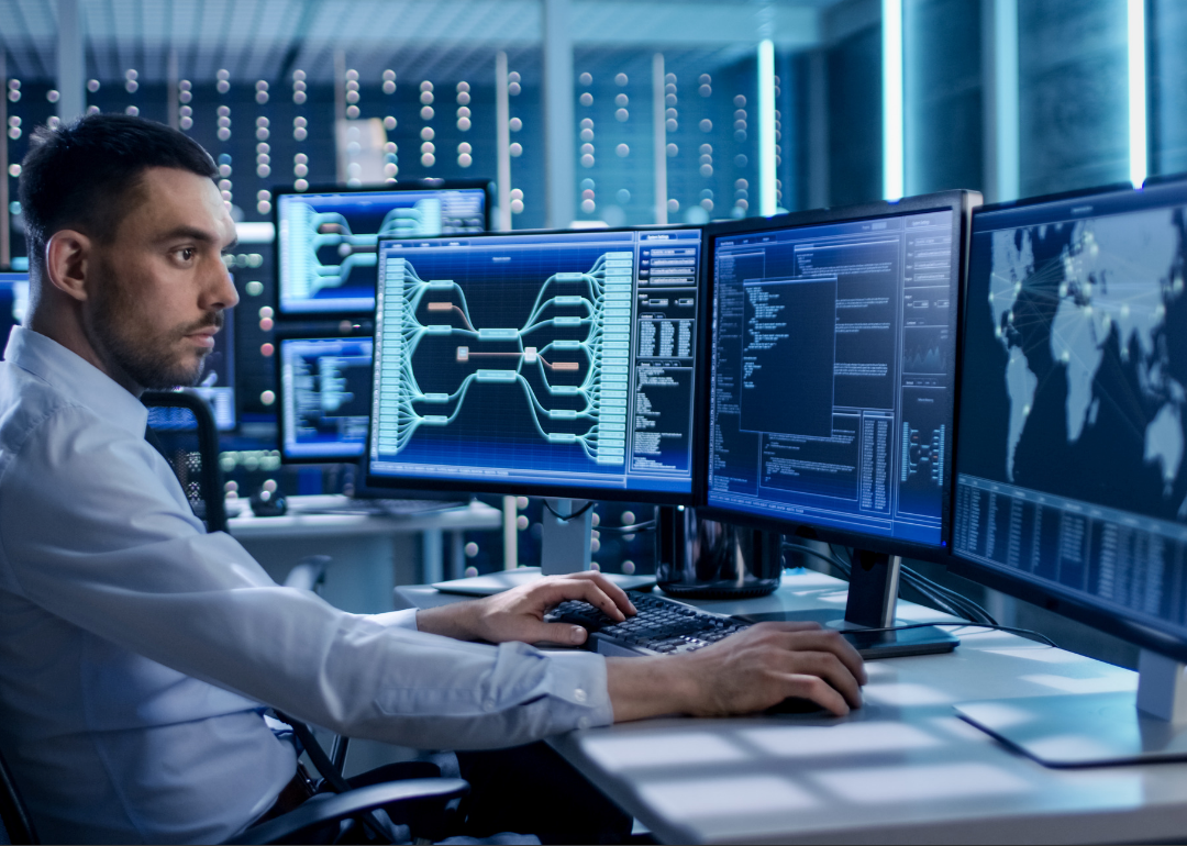 A man working on multiple computer screens in a server room.