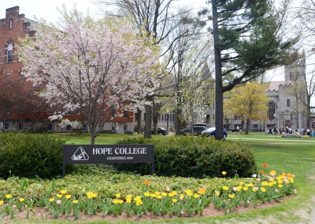 A sign for Hope College surrounded by flowers with historic buildings in the background.