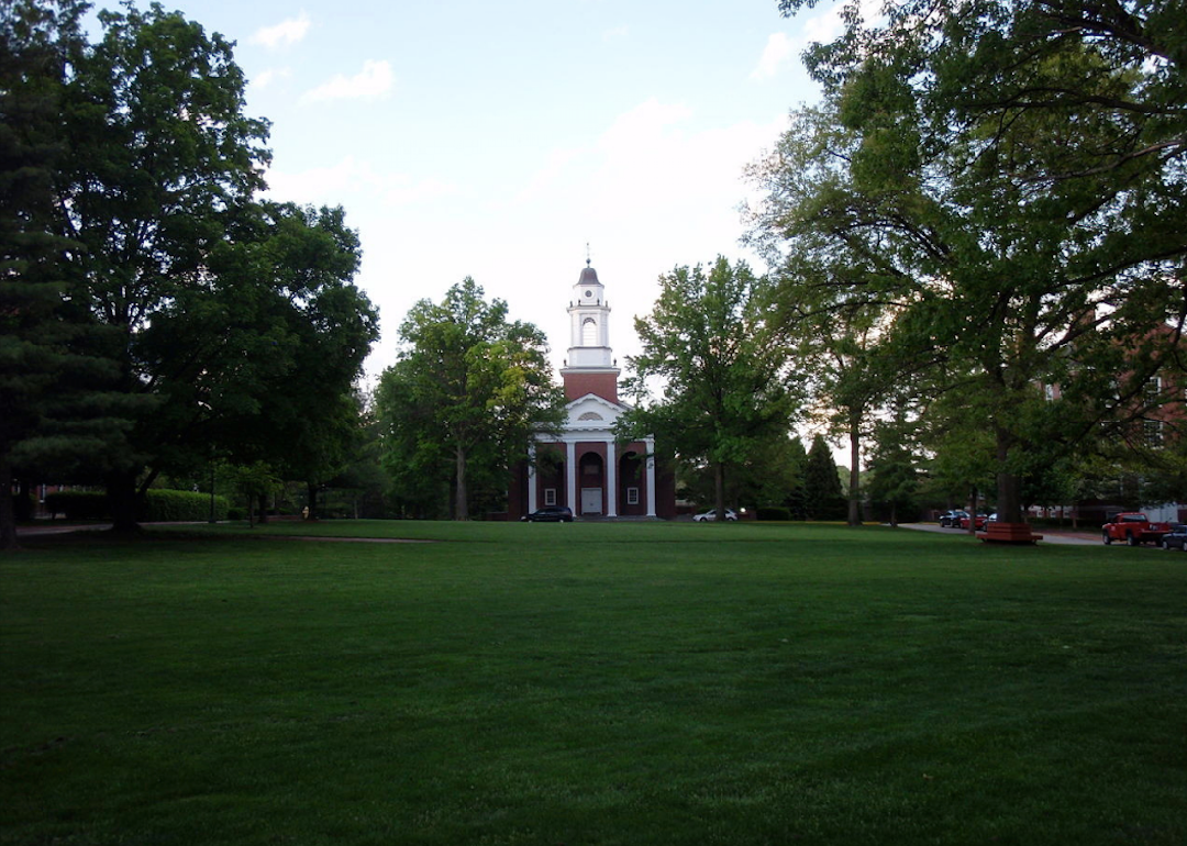 A large green lawn with a red brick building and a tall white clocktower.
