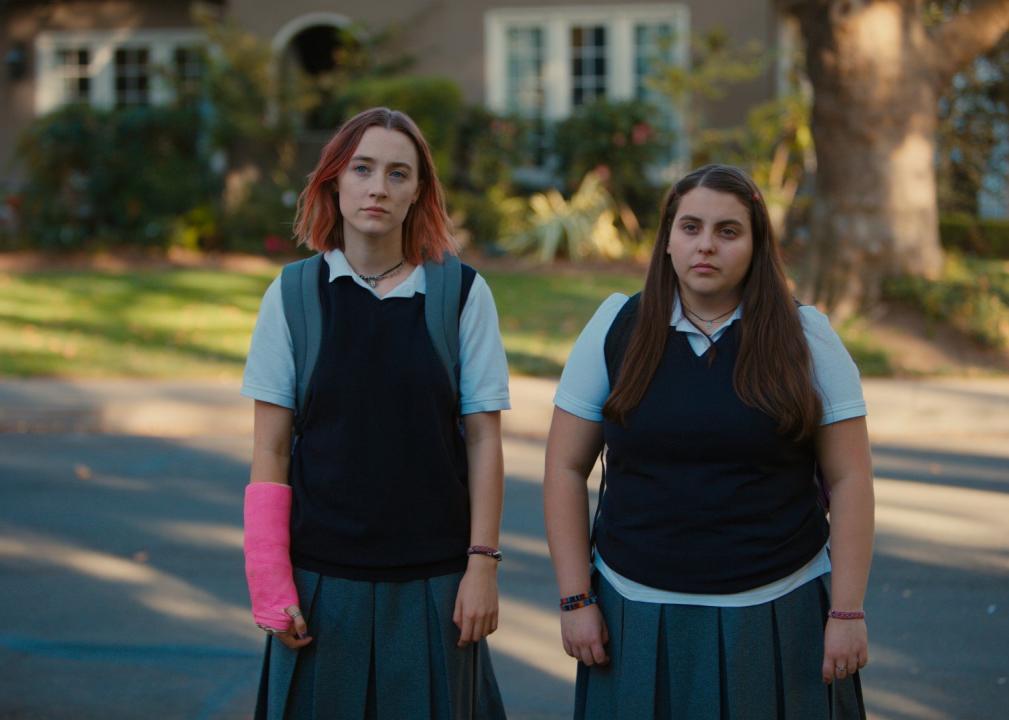 Two girls stare, one with a pink cast on her arm and both wearing school uniforms.