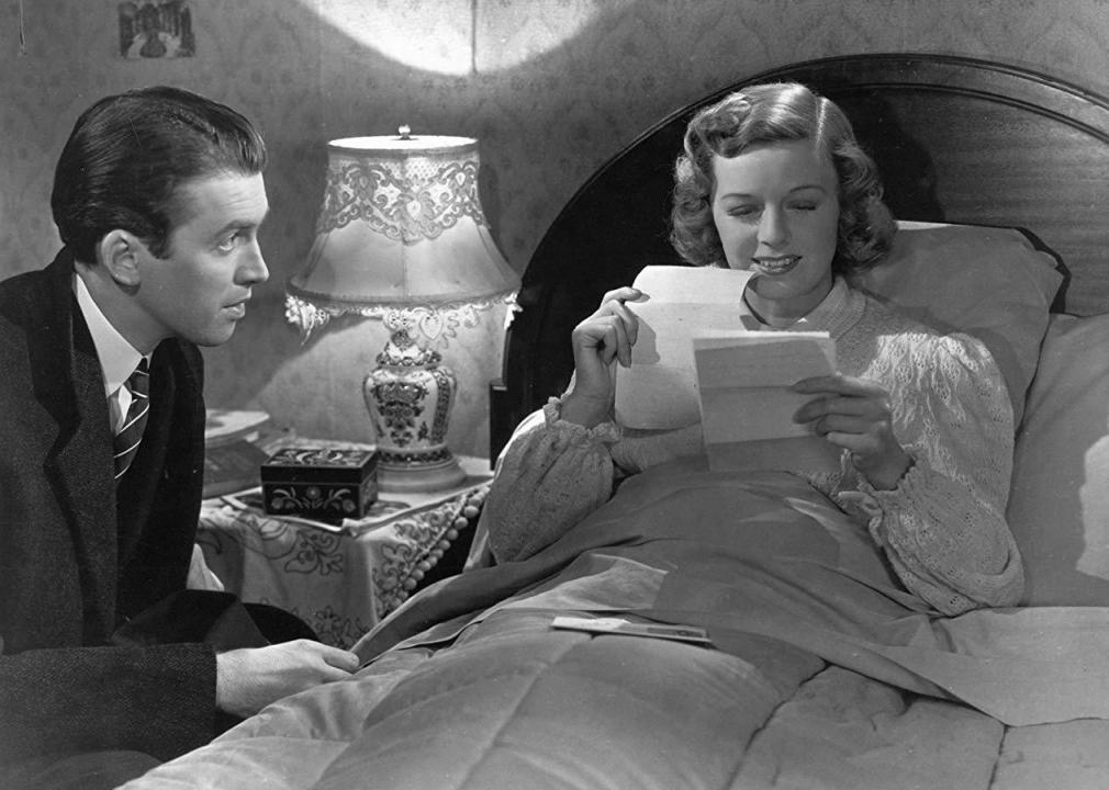 A man sits next to a woman in bed who is reading a letter and smiling.