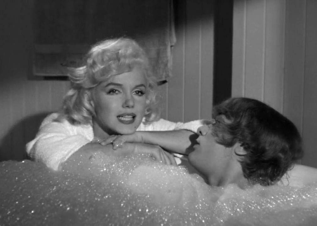 Tony Curtis in a bubble bath and Marilyn Monroe sitting next to the tub talking.