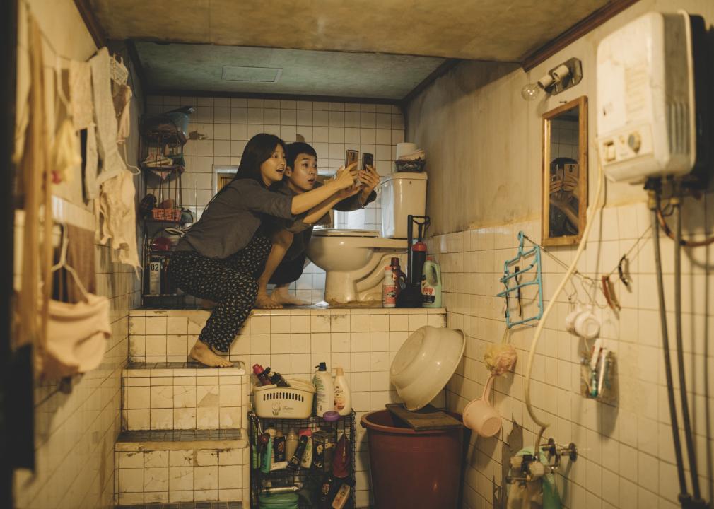 Two young people take selfies in a small, dirty bathroom