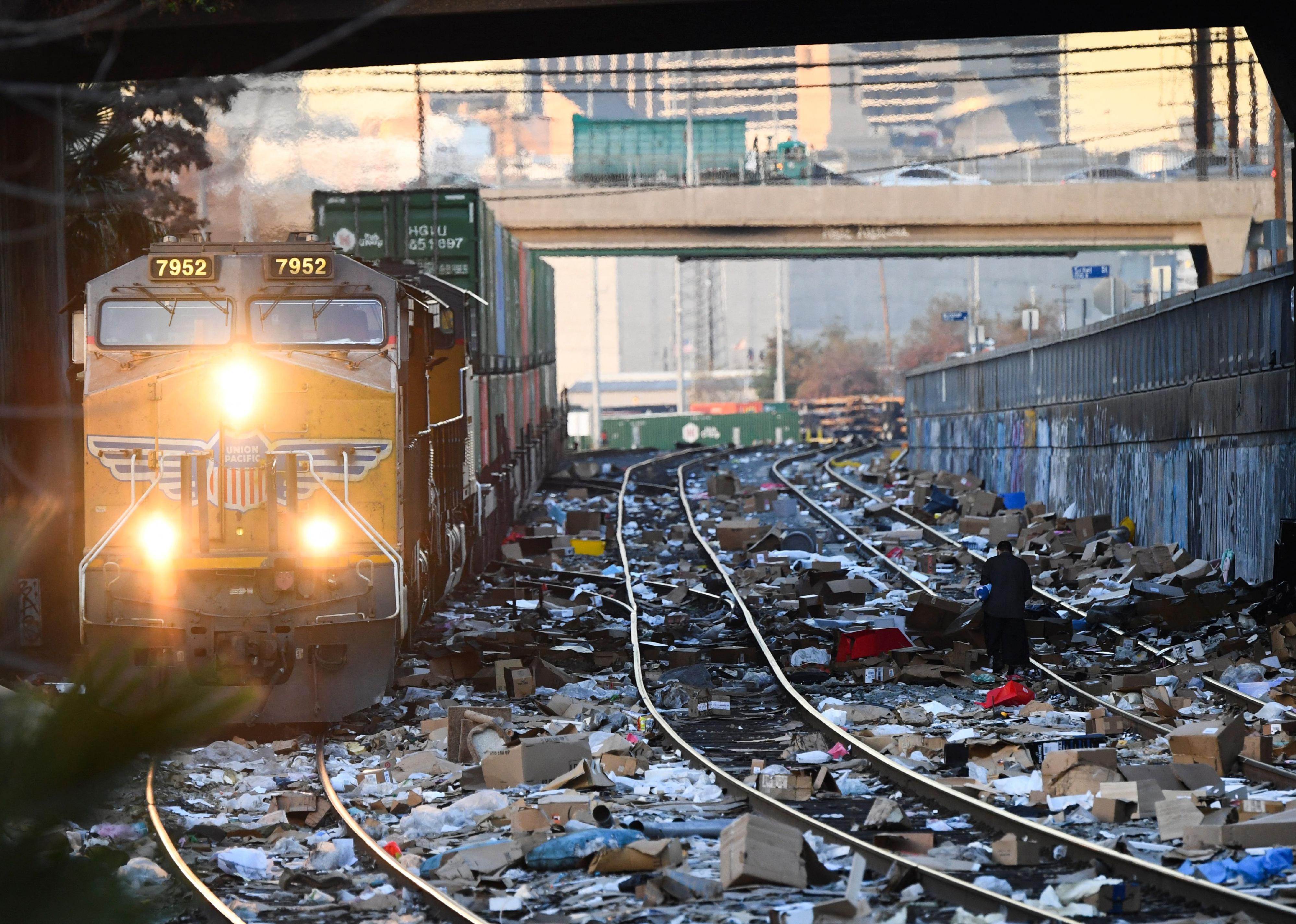 A person carries items collected from the train tracks as a Union Pacific locomotive passes through a section of Union Pacific train tracks littered with thousands of opened boxes and garbage.