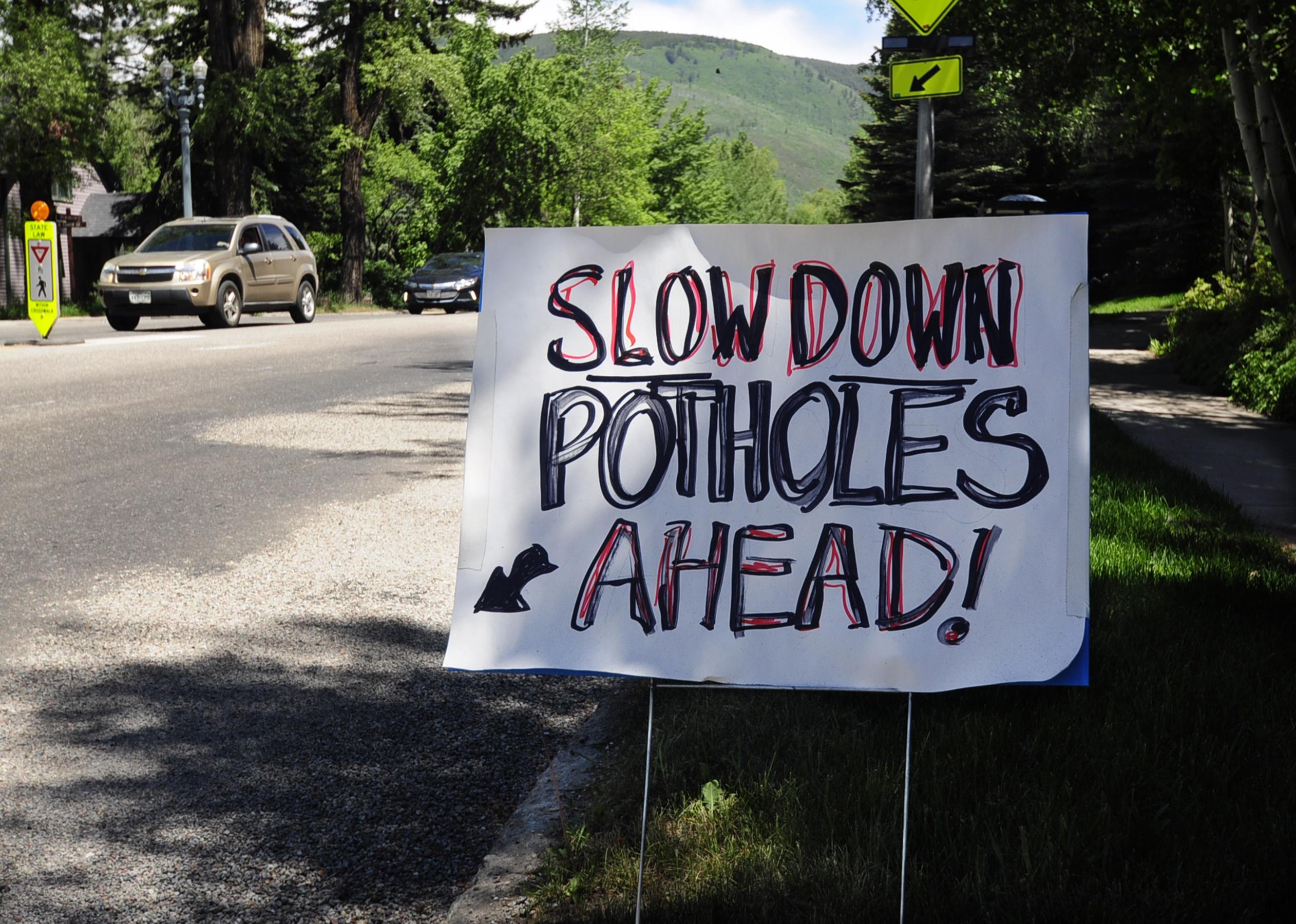 A homemade sign on posterboard warning of potholes in the road.