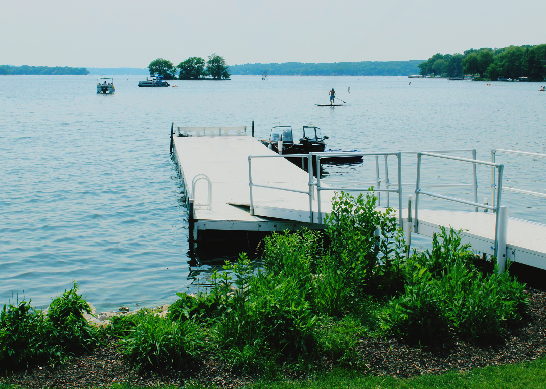 A pier leading out into a lake with a few boats and paddleboarders.