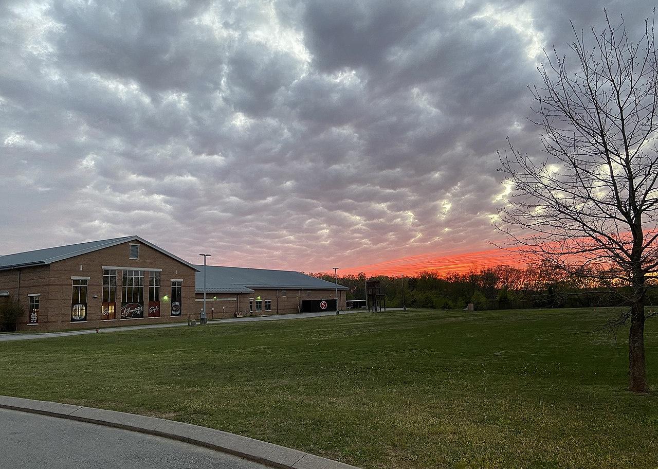 A brown high school building in front of a bright orange sunset.