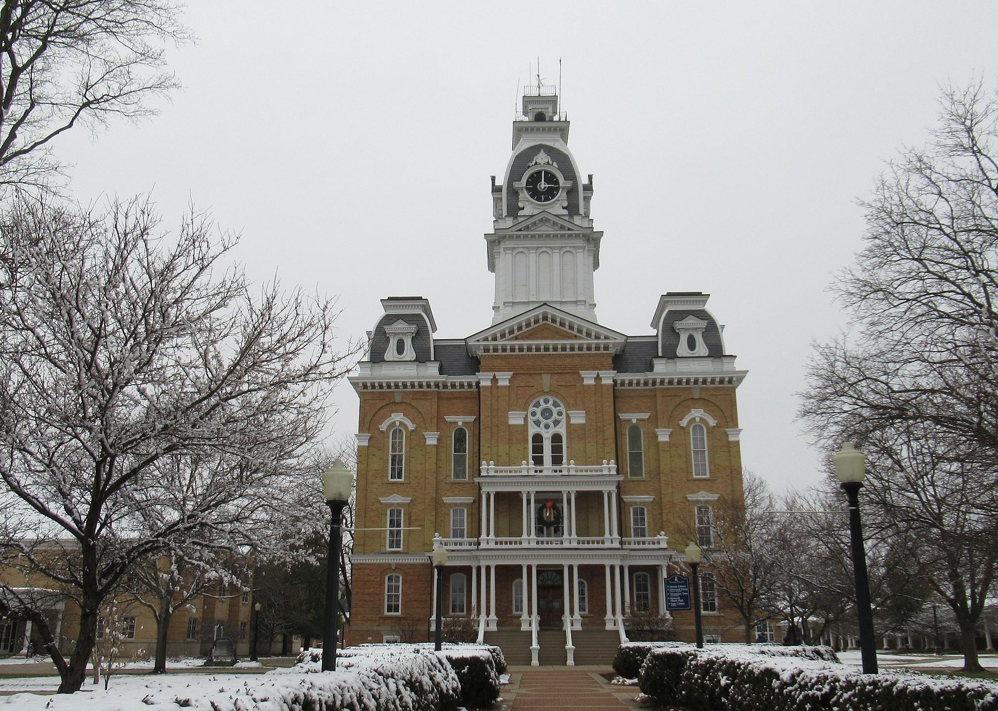 A historic ornate brick building with a clocktower on top in the snow.