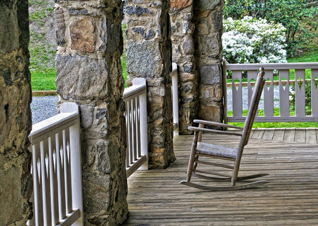 A rocking chair on a porch with stone pillars.