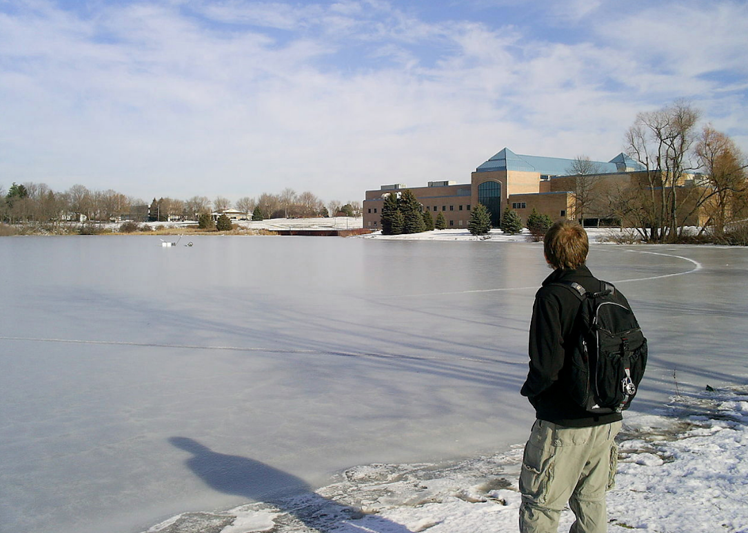 A student looking at a frozen lake in front of Cornerstone University.