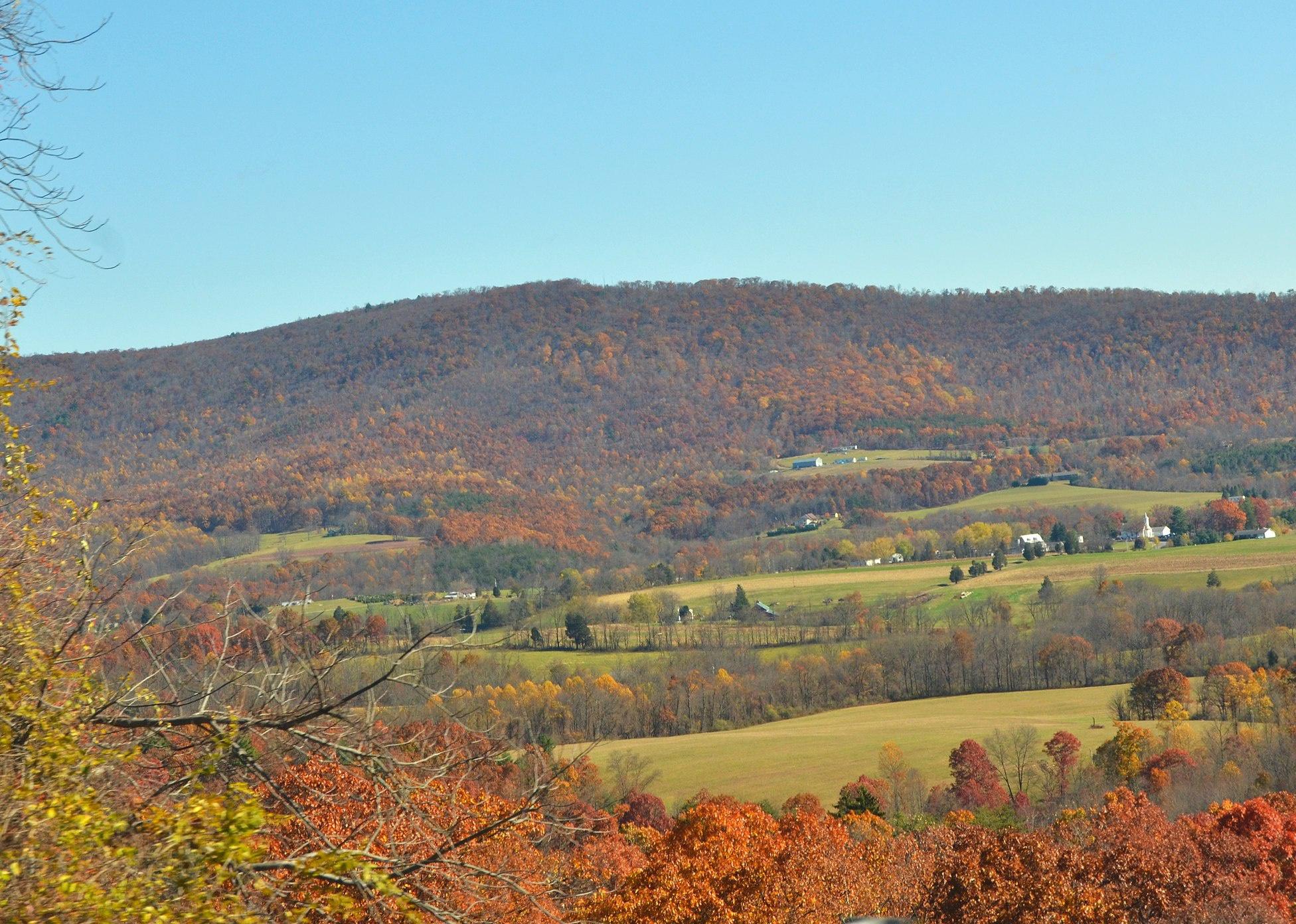 Homes and farms spread out on a Fall colored hillside.