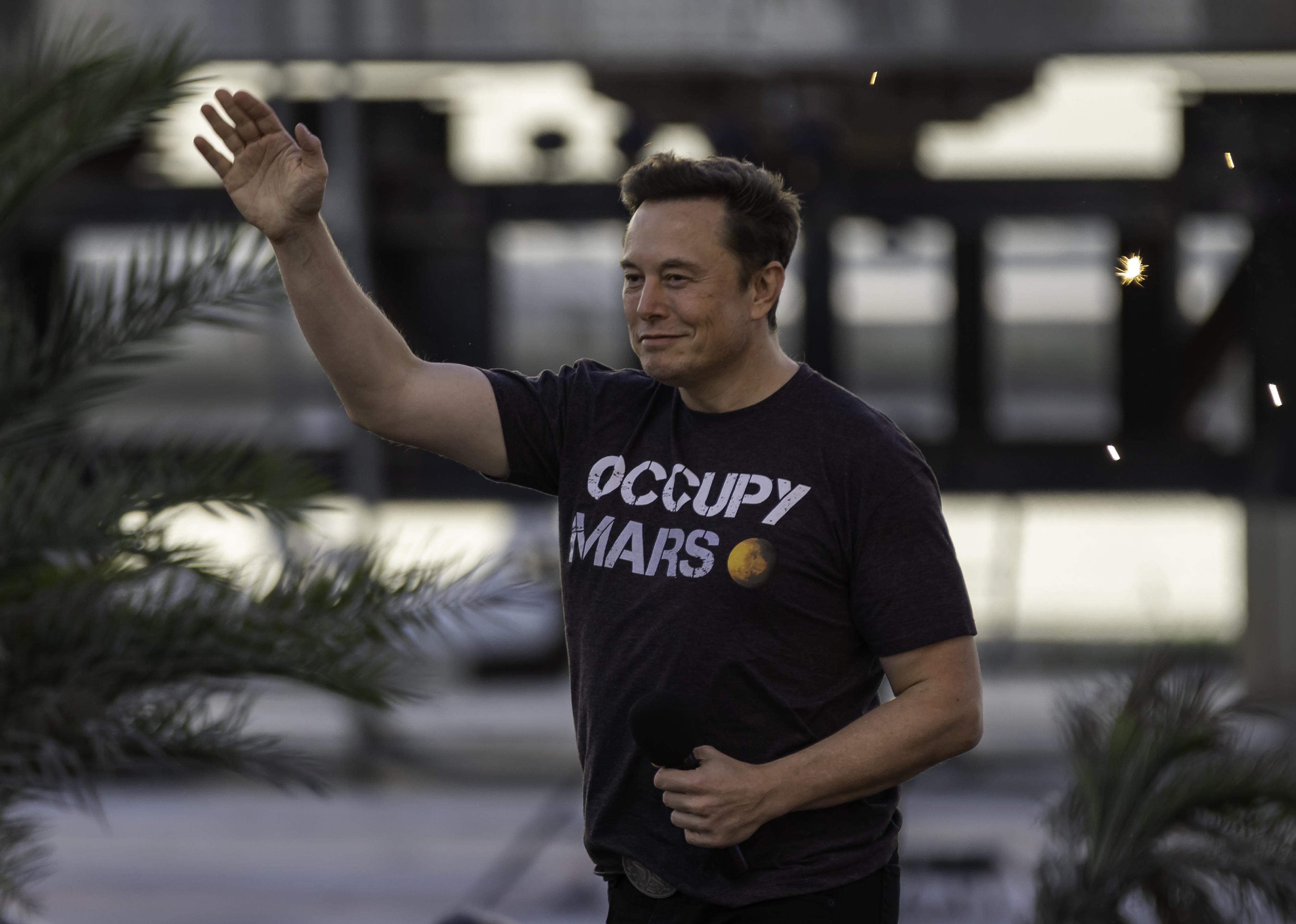 Elon Musk wearing an Occupy Mars t-shirt and waving.