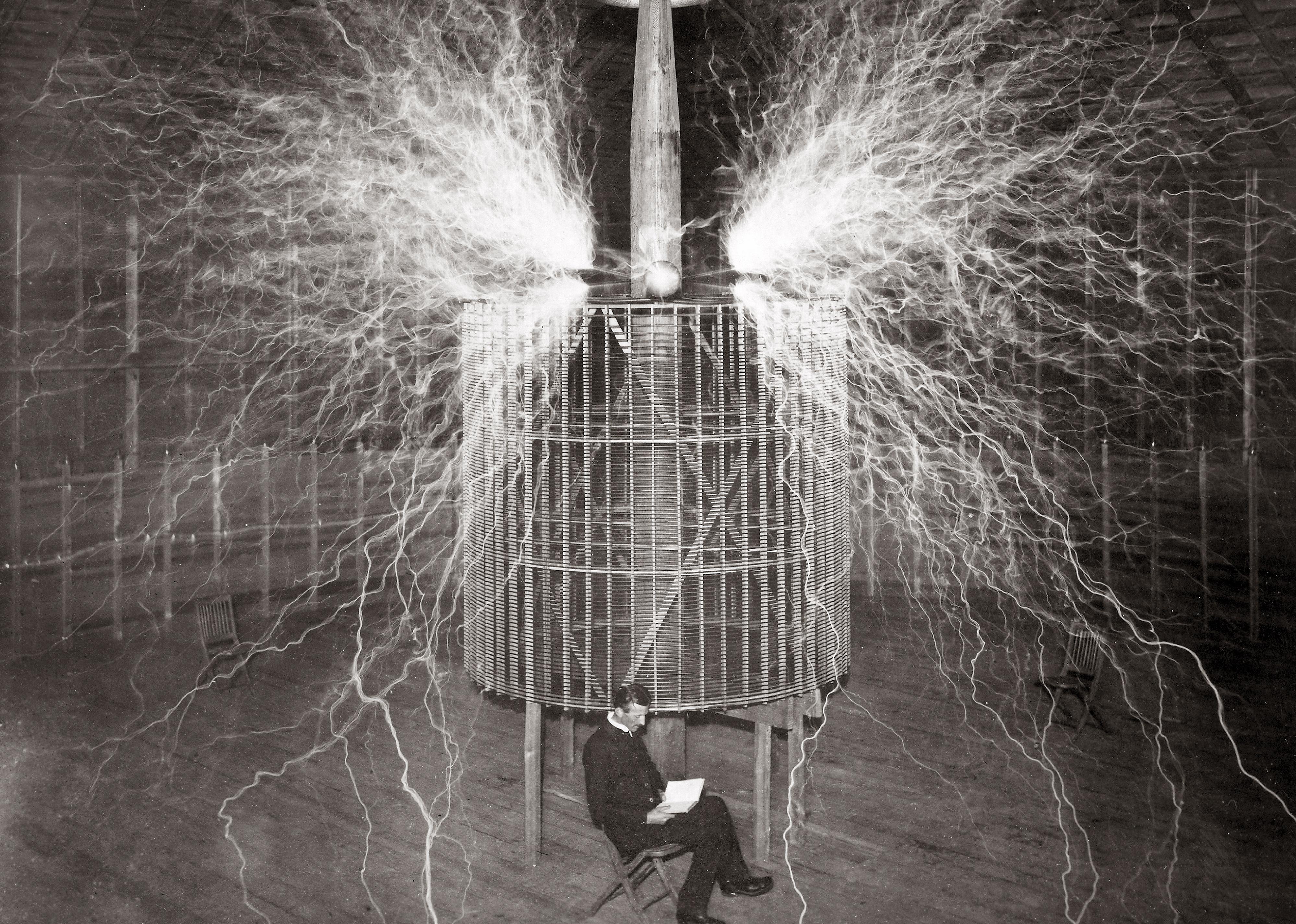 Nikola Tesla sitting in a chair in his lab in front of a contraption shooting electricity from all sides.