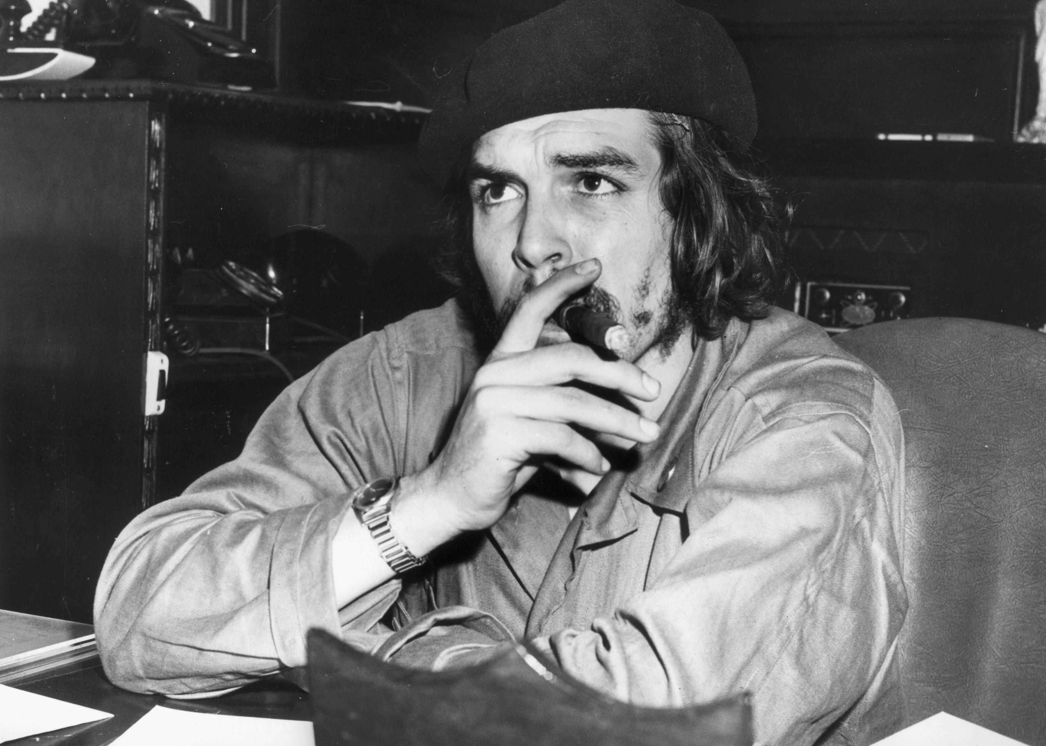 Che Guevara sitting at a desk smoking a cigar.