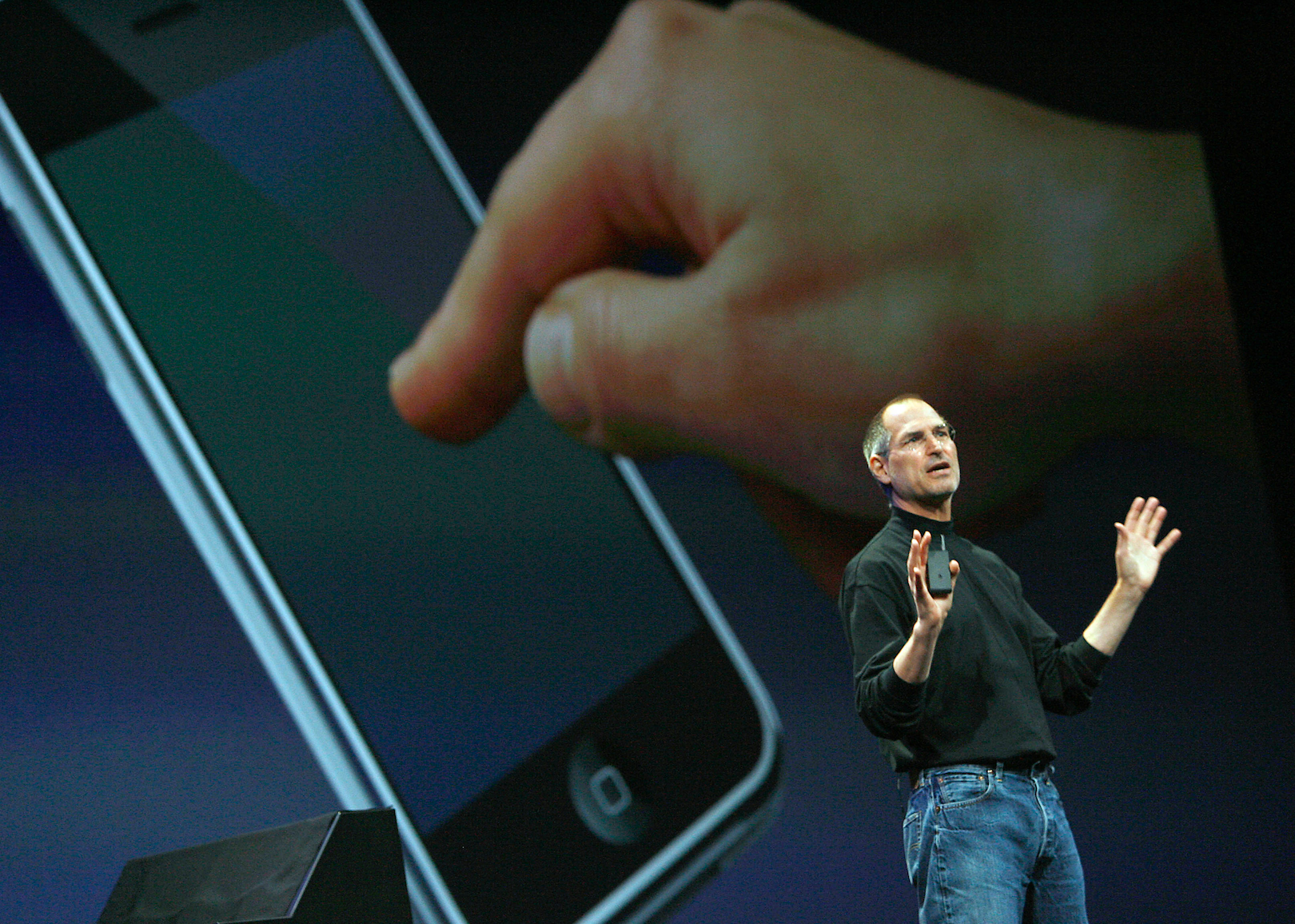 Steve Jobs in a black turtleneck and jeans onstage in front of the iphone.