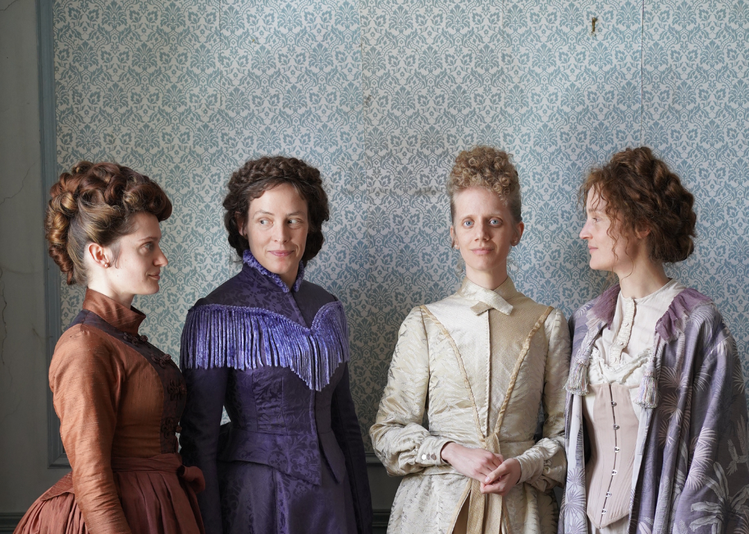 Four women in late 1800s era gowns.