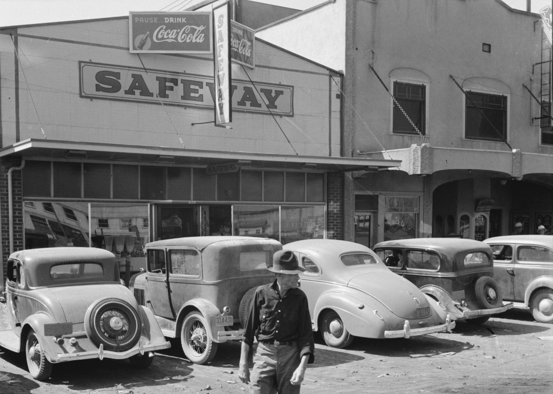 A man walking in front of a grocery store advertising Coca-Cola circa 1900.