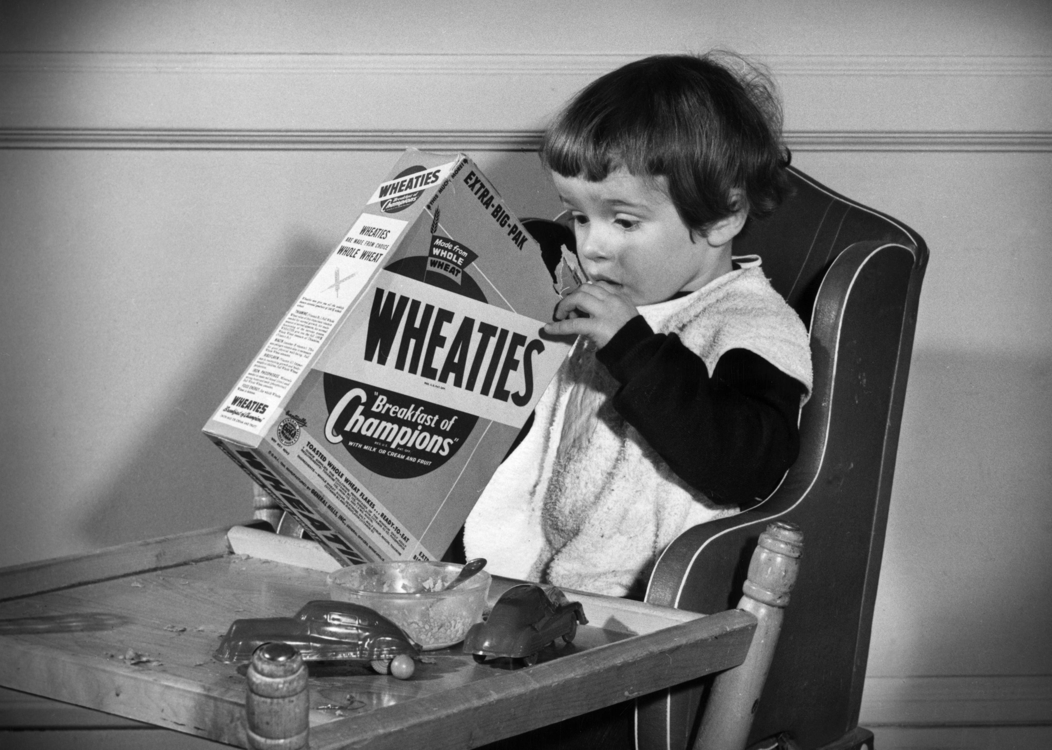 A young child opening a box of Wheaties.