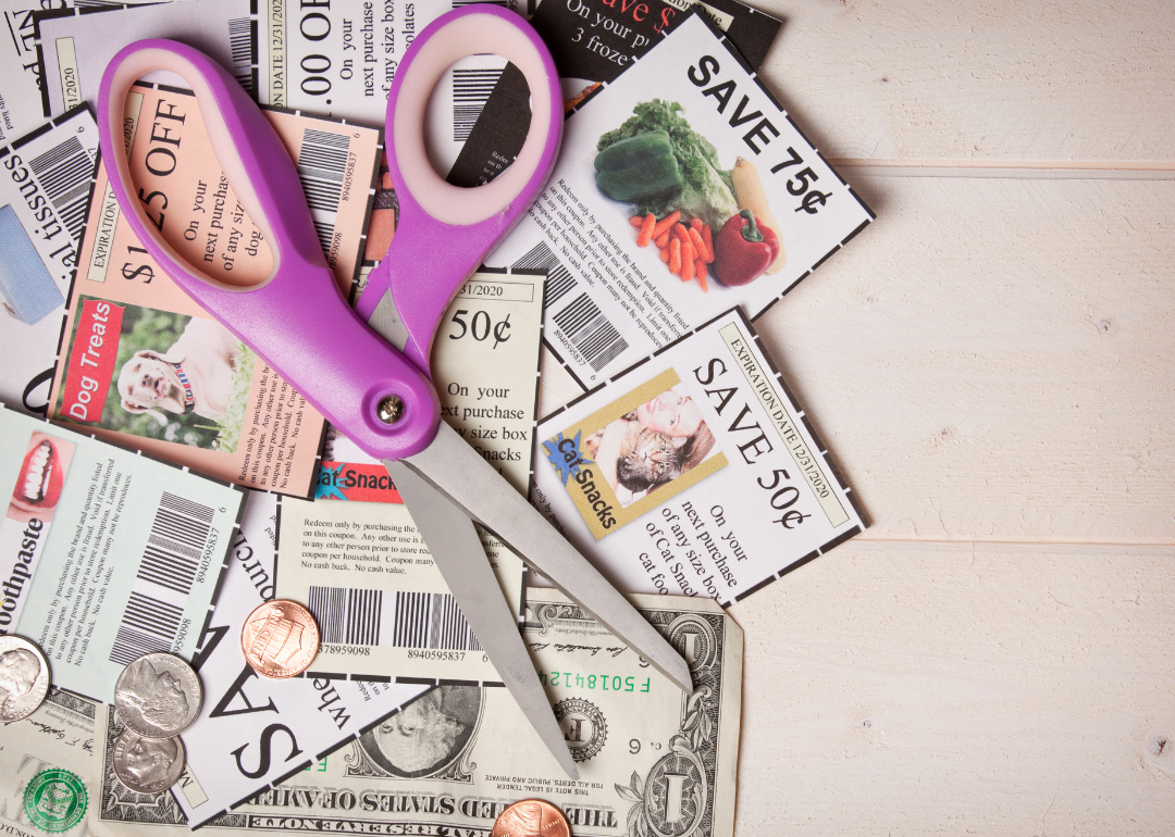 A pile of coupons with scissors and money on a table.
