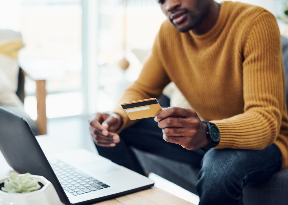 A man looking at his credit card in front of a laptop.