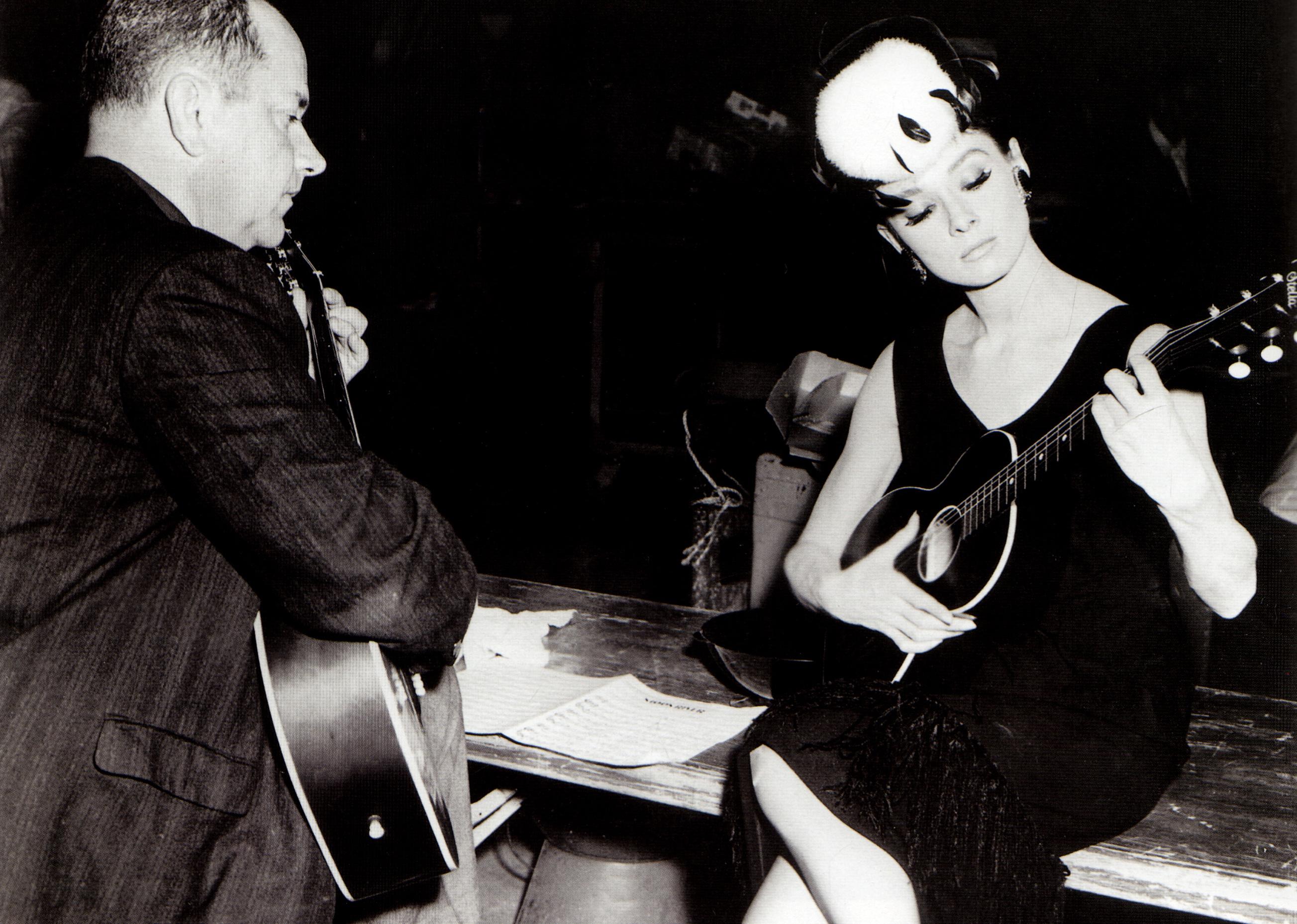 Henry Mancini and Audrey Hepburn playing guitars together.