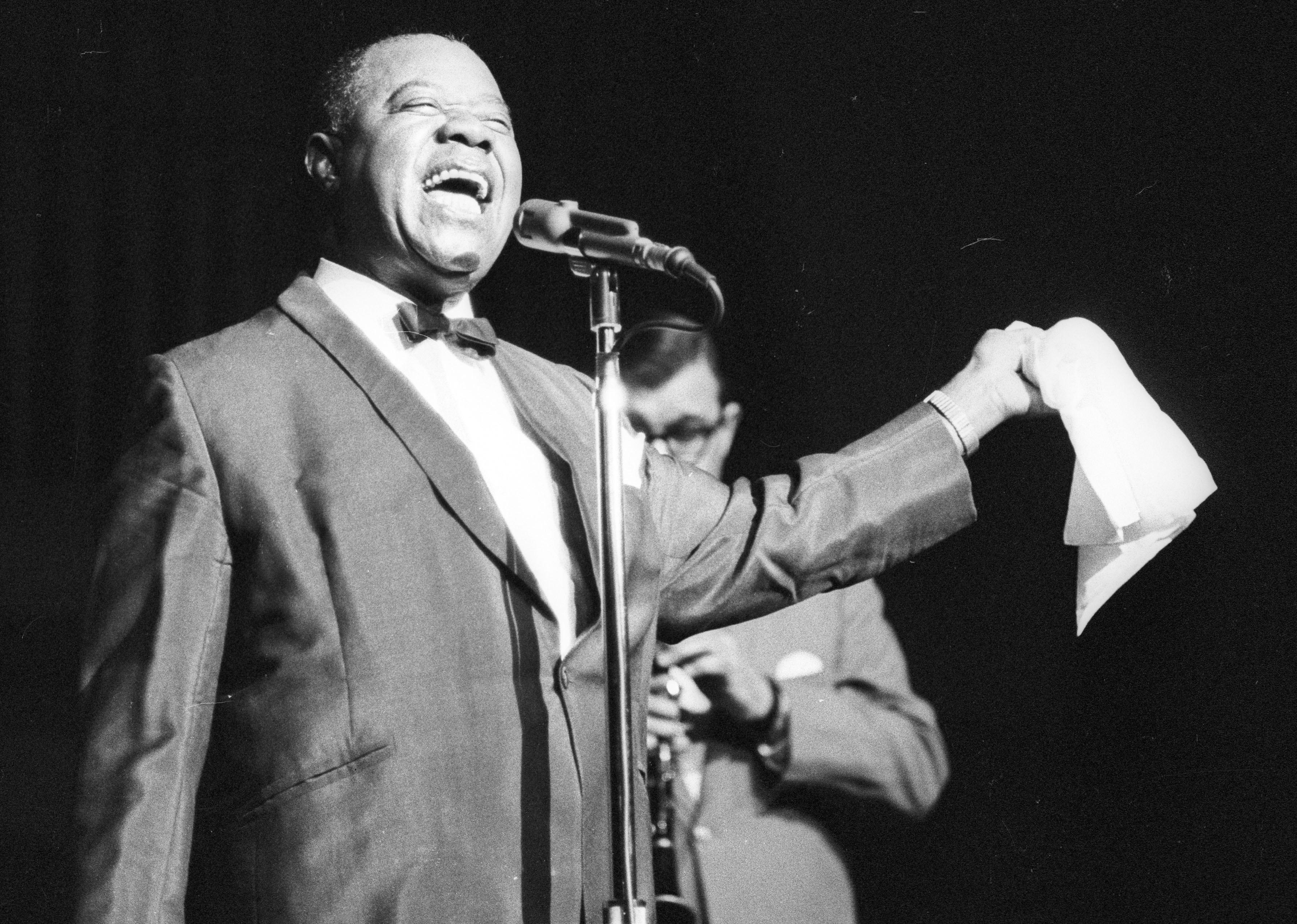 Louis Armstrong in a suit singing onstage.