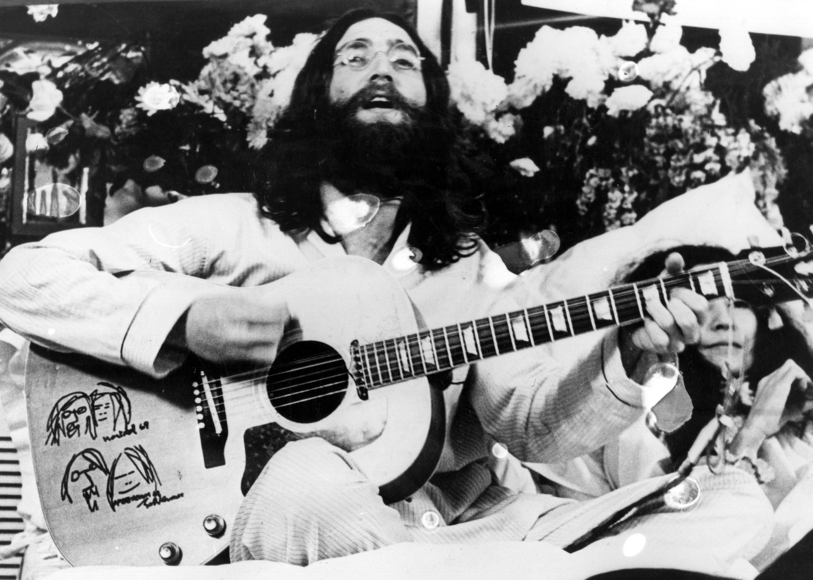 John Lennon playing guitar and singing with Yoko Ono in the background.